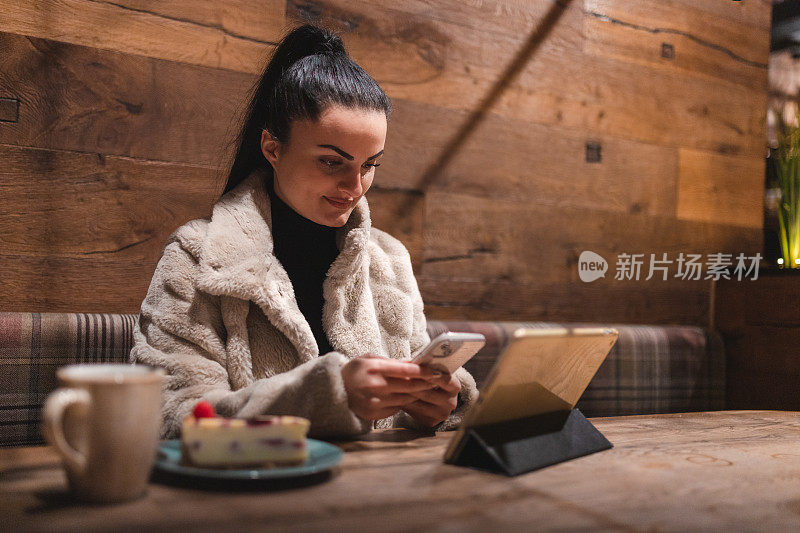 Young businesswoman using her phone and digital tablet in a café